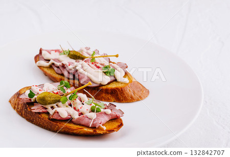 Two delicious bruschetta with meat sauce and capers lying on white plate Two delicious bruschetta with meat sauce and capers lying on white plate 132842707
