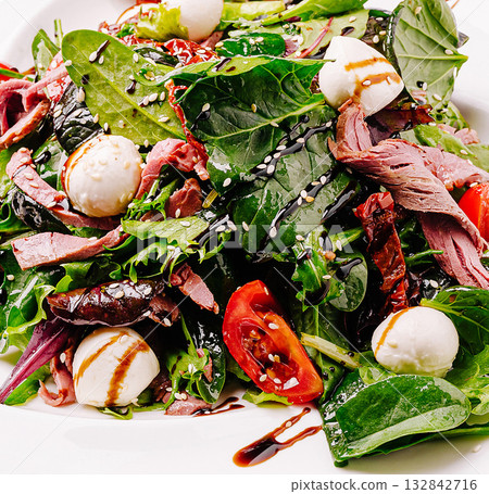 Fresh salad with greens, mozzarella, and roasted meat served in a restaurant 132842716