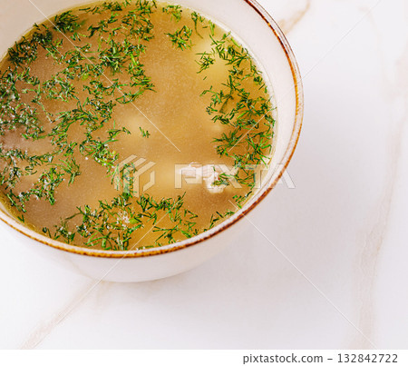 Warm broth with fresh herbs garnished on a marble countertop in a cozy kitchen 132842722