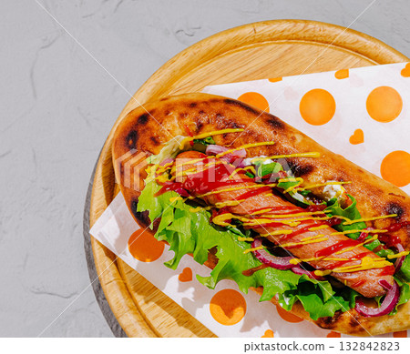 Delicious hot dog served with fresh vegetables and condiments on wooden platter Delicious hot dog served with fresh vegetables and condiments on wooden platter 132842823