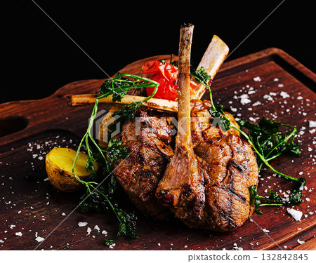 Juicy lamb chops garnished with herbs and vegetables served on wooden board Juicy lamb chops garnished with herbs and vegetables served on wooden board 132842845