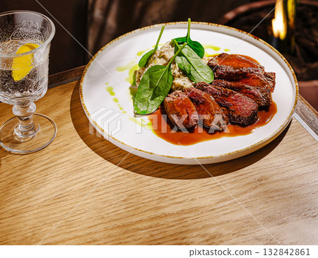Deliciously prepared beef dish with fresh spinach near a glass of water 132842861