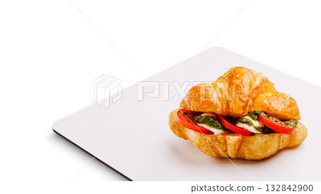Fresh croissant with pesto, tomatoes, and mozzarella served on a plate Fresh croissant with pesto, tomatoes, and mozzarella served on a plate 132842900