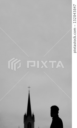 A dramatic, vertical silhouette of a man standing before a large cross on a church structure. man standing at cross church vertical reel. Religious stories or reels 132843847
