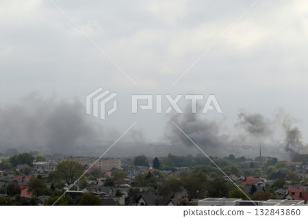 A stark, desolate landscape over a city in Ukraine. Thick, dark smoke billows into the grey sky from a major fire. Fire in Ukraine. Ukraine war smoke city fire A stark, desolate landscape over a city in Ukraine. Thick, dark smoke billows into the grey sky from a major fire. Fire in Ukraine. Ukraine war smoke city fire 132843860