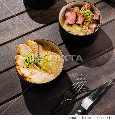 Gourmet chicken and beef soup bowls served on a wooden table 132844312