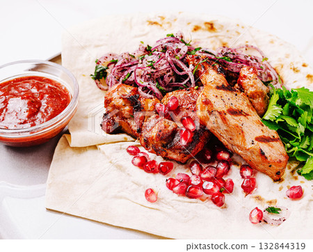 Delicious grilled meat served with pomegranate and fresh herbs on flatbread Delicious grilled meat served with pomegranate and fresh herbs on flatbread 132844319