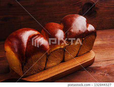 Freshly baked bread loaves on a wooden cutting board in warm lighting 132844327