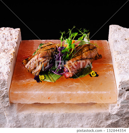 Grilled meat served on a salt block with fresh herbs and garnishes 132844354