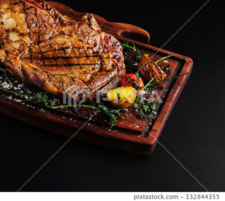 Savory grilled steak served on wooden board with garnishes Savory grilled steak served on wooden board with garnishes 132844355