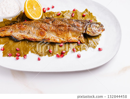 Grilled fish served on grape leaves with pomegranate seeds and lemon Grilled fish served on grape leaves with pomegranate seeds and lemon 132844458