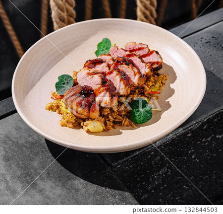 Delicious grilled duck pieces served on a plate with flavorful rice on a table Delicious grilled duck pieces served on a plate with flavorful rice on a table 132844503