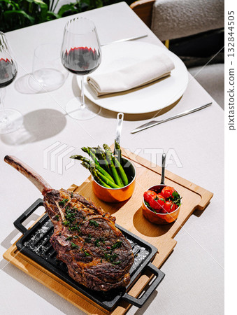 Delicious grilled ribeye steak served with asparagus and tomatoes on a table 132844505