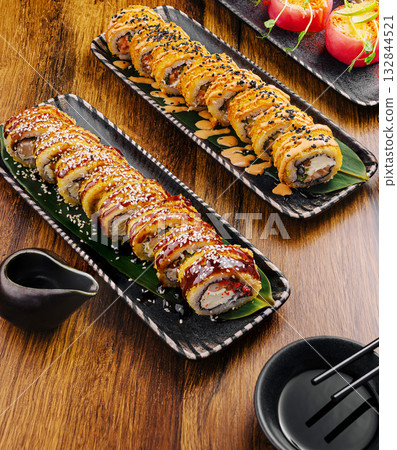 Sushi rolls on black plates with sauce on a wooden table 132844521