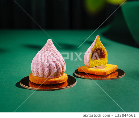 Two exquisite pastries sit elegantly on gold bases against a deep green surface 132844561