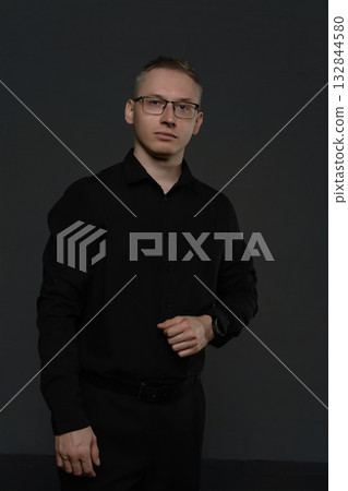 Young man in a formal black outfit poses confidently against a dark background Young man in a formal black outfit poses confidently against a dark background 132844580