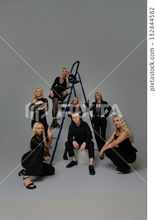 Group of stylish people posing creatively around a ladder for a photoshoot in a studio Group of stylish people posing creatively around a ladder for a photoshoot in a studio 132844582