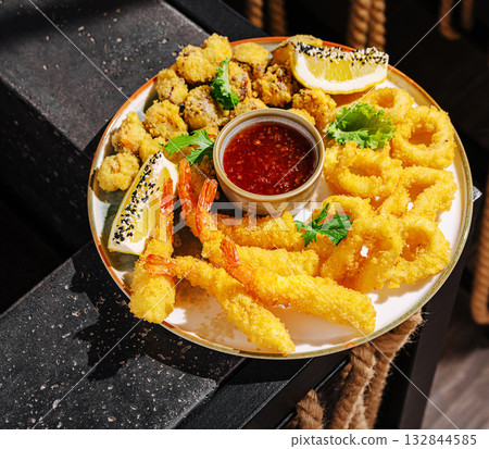 Fried seafood platter with shrimp, calamari, and dip in a lively setting Fried seafood platter with shrimp, calamari, and dip in a lively setting 132844585