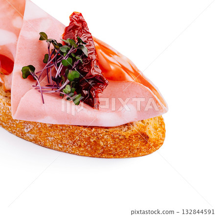 Savory appetizer featuring cured meat on toasted bread with garnishes 132844591