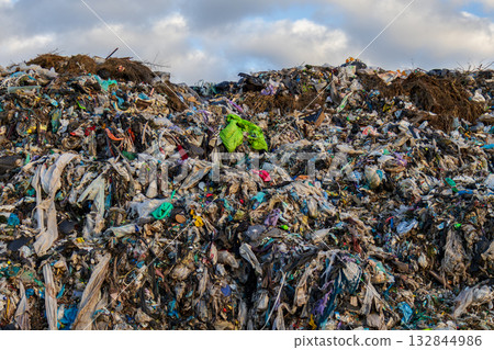 A large landfill site displays a chaotic mix of plastic waste, garbage, and organic matter under a cloudy sky, highlighting pollution issues 132844986