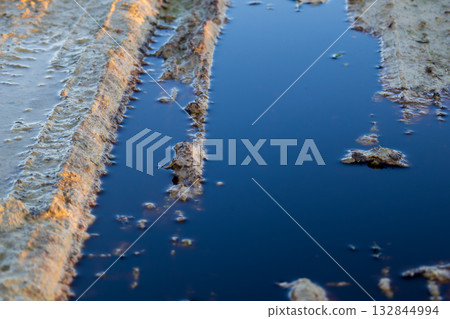 Dark, polluted water collects in muddy tire tracks, highlighting the detrimental effects of waste on the surrounding ecology and environment Dark, polluted water collects in muddy tire tracks, highlighting the detrimental effects of waste on the surrounding ecology and environment 132844994