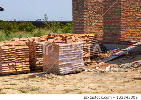 Bricks are neatly stacked on a construction site, prepared for building homes in a growing neighborhood under clear skies Bricks are neatly stacked on a construction site, prepared for building homes in a growing neighborhood under clear skies 132845002