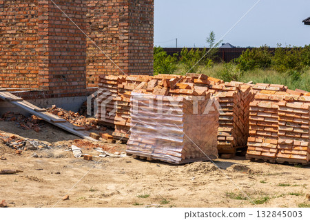 Bricks neatly stacked on pallets at a construction site, indicating ongoing development of new housing in a suburban location 132845003