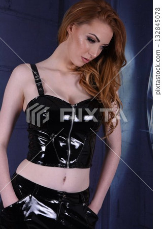 Tall, beautiful, redhead model in black PVC outfits, posing by the window in an old house 132845078