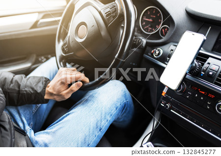 A man drives a car with a modern black leather interior. An autumn cityscape is visible outside the window. A man drives a car with a modern black leather interior. An autumn cityscape is visible outside the window. 132845277