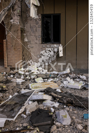 Ground level view of structural destruction broken concrete insulation, shattered glass and scattered documents surround damaged wall with exposed bricks and hanging fixture near broken window. 132845459