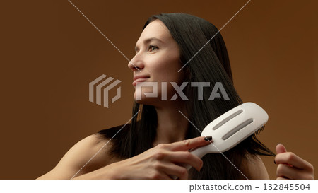 Woman brushing long straight hair with white detangling brush smiling calmly 132845504