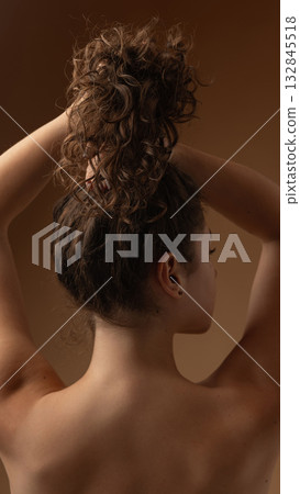 Woman holding curly hair in hands above head showing strength and texture of natural beauty Woman holding curly hair in hands above head showing strength and texture of natural beauty 132845518
