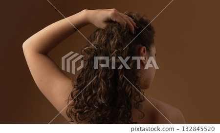 Woman touching curly hair showing natural volume and softness from scalp care Woman touching curly hair showing natural volume and softness from scalp care 132845520