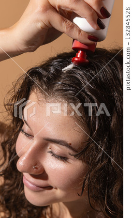 Female model applying lotion directly onto scalp for hair restoration care Female model applying lotion directly onto scalp for hair restoration care 132845528