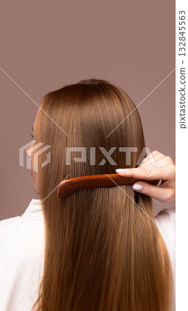Woman combing long straight hair with wooden brush on neutral background 132845563