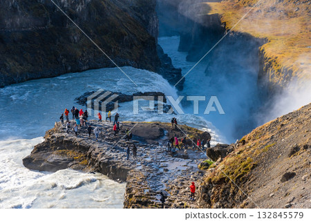 Gullfoss waterfall in Iceland showcases powerful cascades flowing into a canyon. Visitors admire the natural beauty from nearby viewpoints, especially during sunny weather. Gullfoss waterfall in Iceland showcases powerful cascades flowing into a canyon. Visitors admire the natural beauty from nearby viewpoints, especially during sunny weather. 132845579