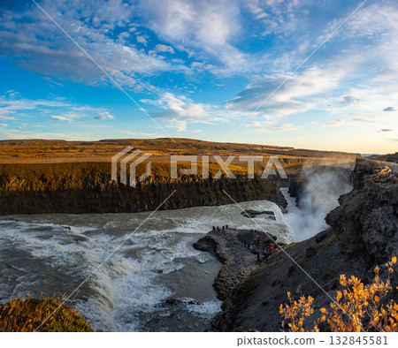 Gullfoss waterfall in Iceland showcases powerful cascades flowing into a canyon. Visitors admire the natural beauty from nearby viewpoints, especially during sunny weather. 132845581