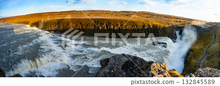 Gullfoss waterfall in Iceland showcases powerful cascades flowing into a canyon. Visitors admire the natural beauty from nearby viewpoints, especially during sunny weather. 132845589