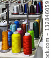 Brightly colored spools of thread arranged neatly in a sewing workshop with machines in the background 132846059