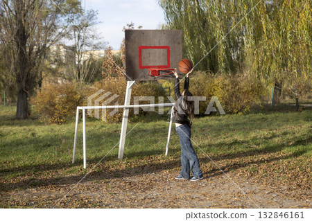 A teenage girl throws a ball into a basketball hoop on an outdoor sports court. A teenage girl throws a ball into a basketball hoop on an outdoor sports court. 132846161
