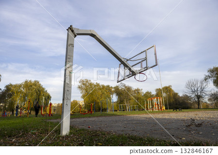 A broken and lopsided basketball hoop stands on an open-air sports court A broken and lopsided basketball hoop stands on an open-air sports court 132846167
