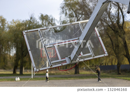 A broken and lopsided basketball hoop stands on an open-air sports court A broken and lopsided basketball hoop stands on an open-air sports court 132846168