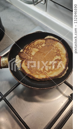 Golden brown pancake cooking in a frying pan on a gas stove. Concept of homemade breakfast, comfort food and cozy morning routine Golden brown pancake cooking in a frying pan on a gas stove. Concept of homemade breakfast, comfort food and cozy morning routine 132846890
