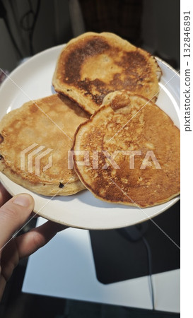 Three golden pancakes served on a white plate held by hand. Concept of homemade breakfast, cozy morning and comfort food simplicity Three golden pancakes served on a white plate held by hand. Concept of homemade breakfast, cozy morning and comfort food simplicity 132846891