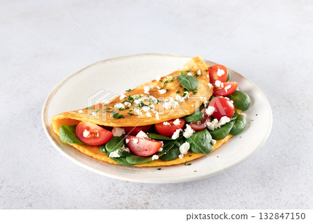 Stuffed omelette with tomatoes, cheese and spinach on a white background.  132847150