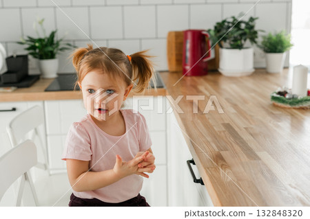 Preschool girl talking animatedly in the kitchen, copy space. Communication, self-expression, and emotional development in the safe and familiar space of home. 132848320