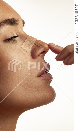 Side view of woman touching nose with adhesive strip after cosmetic care procedure Side view of woman touching nose with adhesive strip after cosmetic care procedure 132848807