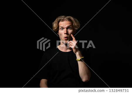 Surprised man in black shirt with wide eyes and shocked expression under dramatic light 132849731