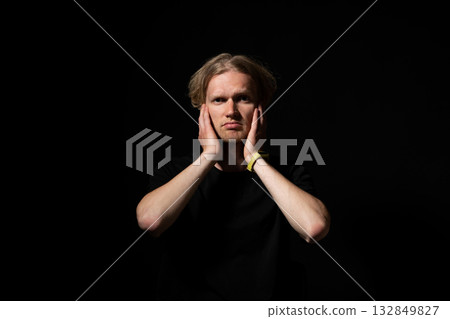 Man in black shirt touching face with both hands in moment of realization under dramatic lighting Man in black shirt touching face with both hands in moment of realization under dramatic lighting 132849827