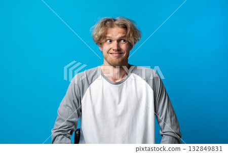 Awkward man in gray and white shirt smiling nervously and looking sideways on blue background Awkward man in gray and white shirt smiling nervously and looking sideways on blue background 132849831
